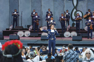 Mariachi singer in a blue suit performs on stage with the band and cheering crowd in front of him.
