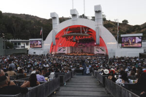 Outdoor concert at John Williams Stage with a red-lit semicircular arch and a packed audience watching performers on stage.