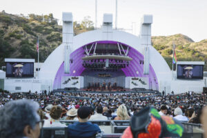 Outdoor concert at John Williams Stage with a large crowd and a purple-lit curved stage.