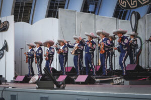 Mariachi band in blue outfits with sombreros performing on a stage, playing violins and guitars.